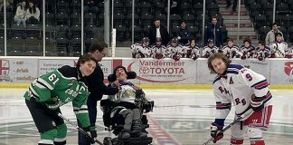 Five Counties Children's Centre CEO Scott Pepin hands the puck over to Five Counties alumnus Nick Scarr, who prepares to do the ceremonial puck drop before the Cobourg Cougars home game on November 20, 2023, which helped raise funds for the charitable organization serving children with special needs in the greater Kawarthas region. During his time at Five Counties, the centre's augmentative communication team set up Nick with a tablet to help him better communicate. (Photo courtesy of Five Counties)