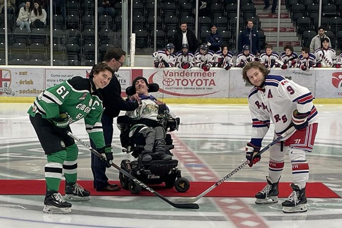 Five Counties Children's Centre CEO Scott Pepin hands the puck over to Five Counties alumnus Nick Scarr, who prepares to do the ceremonial puck drop before the Cobourg Cougars home game on November 20, 2023, which helped raise funds for the charitable organization serving children with special needs in the greater Kawarthas region. During his time at Five Counties, the centre's augmentative communication team set up Nick with a tablet to help him better communicate. (Photo courtesy of Five Counties)