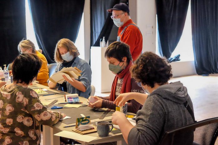 Artist Jeffrey Macklin (standing) leading a book binding workshop at Artspace in February 2023 prior to the artist-run centre's Book + Zine Fest. For decades, Macklin has supported emerging artists by leading workshops on graphic design and printmaking with Artspace, the Electric City Culture Council, and Art Gallery of Peterborough. Macklin believes that art should not be kept a secret, and there is strength in creating a community of artists. (Photo: Artspace)