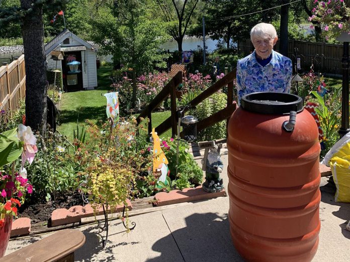 Peterborough resident Ellie Dustler stands behind a rain barrel acquired from the GreenUP Store and Resource Centre. A rain barrel acts as an all-season water conservation tool. By collecting rain water, residents can save money, improve how indoor and outdoor plants are watered, and help reduce the pressure on the local municipal stormwater system during flooding events. (Photo: Melynda Dustler)