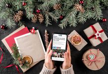 Hands holding a smartphone displaying kawarthaNOW's 2023 holiday hours listing with a Christmas scene in the background. (Photo: kawarthaNOW)