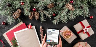 Hands holding a smartphone displaying kawarthaNOW's 2023 holiday hours listing with a Christmas scene in the background. (Photo: kawarthaNOW)