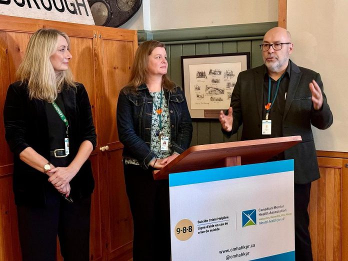 Canadian Mental Health Association Haliburton, Kawartha, Pine Ridge (CMHA HKPR) CEO Mark Graham (right) speaks about the new 988 suicide crisis helpline at a media event on November 17, 2023 with program and services director Tracy Graham (left) and corporate services director Ellen Watkins. According to the association, the number of people dialing the helpline locally since its launch on November 30, 2023 is on the rise. (Photo: CMHA HKPR)