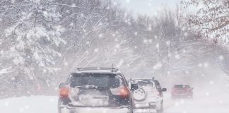 Three cars on a snow-covered road during a winter blizzard. (Stock photo)