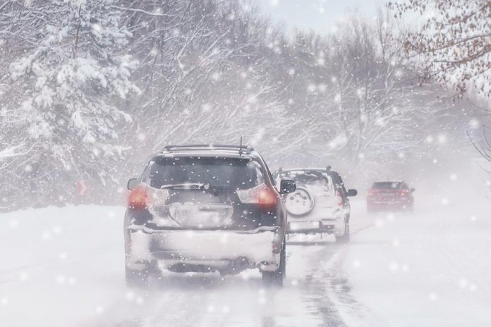 Three cars on a snow-covered road during a winter blizzard. (Stock photo)