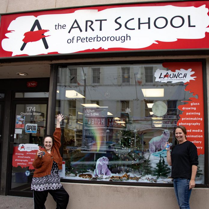 Art School of Peterborough receptionist Raine Knudsen (left) and executive director Jenni Johnston (right) celebrate their win in front of the school's window display, while  holding the handmade ornaments distributed to community members throughout the holiday season. (Photo: Peterborough DBIA)