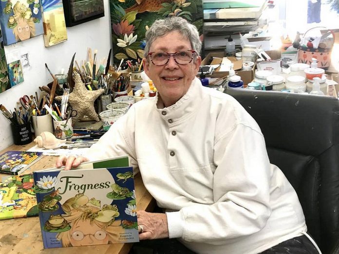 Kawartha Lakes artist Eugenie Fernandes in her studio with "Frogness," a children's book by Sarah Nelson Fernandes illustrated. She will be reading from "Frogness" as well as from her own latest book "When Rabbit Was a Lion" at the Art Gallery of Peterborough's Family Sunday event on February 18, 2024 as part of the Peterborough Snofest celebrations over Family Day long weekend. (Photo: Sarah Nelson)