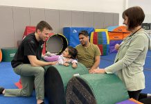 Kawartha Gymnastics coach Nathan (left) gets a smile from two-year-old Mirha as she takes part in a new adaptive gymnastics program at the club. Looking on are Mirha's dad Mansoor and Five Counties Children's Centre recreation therapist Colleen Ristok. (Photo: Five Counties Children's Centre)