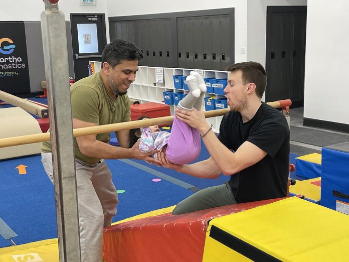 Kawartha Gymnastics coach Nathan (right) helps two-year-old Mirha do a hip pullover on the uneven parallel bars, with an assist from her dad Mansoor. The new adaptive gymnastics program being offered by Kawartha Gymnastics encourages parent participation and gives kids with varying abilities, exceptionalities, and sensory issues an introduction to the sport. (Photo: Five Counties Children's Centre)