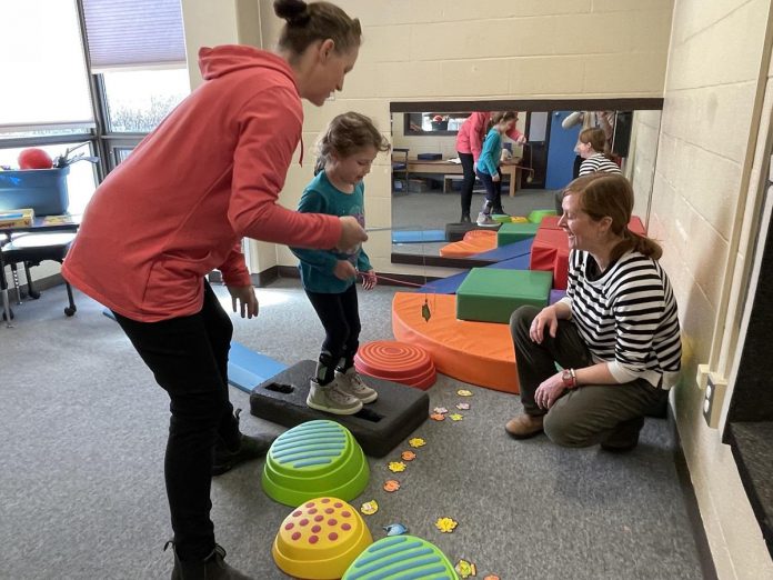 Monica and her daughter Paisley catch the spirit of teamwork during a therapy session with Five Counties Children's Centre clinician Katie (right). Paisley works on her ability to  control movement by stepping up and off different surfaces, in an obstacle course that also challenges her to see if she can 'catch' more fish than her mother.  (Photo courtesy of Five Counties) 