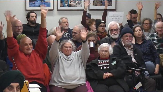 Concerned residents of the Bonnerworth Park neighbourhood wave their hands in lieu of applause in the gallery at Peterborough City Hall during city council's general committee meeting on April 2, 2024, after Town Ward councillor Alex Bierk spoke in support of a motion from Town Ward councillor Joy Lachica to consider alternative locations for the proposed pickleball courts at the park. (kawarthaNOW screenshot of City of Peterborough video)