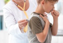 A young boy coughing while being examined by a doctor. (Stock photo)