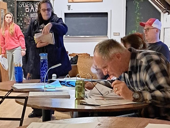 Director Gerry McBride (front right) peers at the script as actors (back, left to right) June Govier, Elaine Day, and Nathan Govier (red cap) prepare for a night of early rehearsals for "Tide of Hope", Trent Valley Archives Theatre's inaugural history play being staged at Market Hall Performing Arts Centre on May 15 and 16, 2024. (Photo courtesy of Trent Valley Archives Theatre)