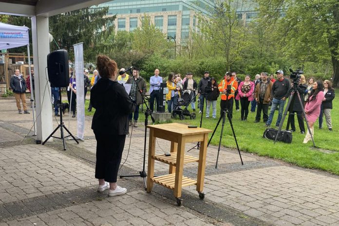 Peterborough Musicfest board chair Tracy Condon at the mic during an announcement of the free-admission outdoor music festival's lineup for its 37th season on May 14, 2024 at Millennium Park. (Photo: Paul Rellinger / kawarthaNOW)