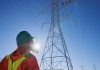 Hydro One worker looking up at other workers on a transmission tower. (Photo: Hydro One)