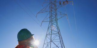 Hydro One worker looking up at other workers on a transmission tower. (Photo: Hydro One)