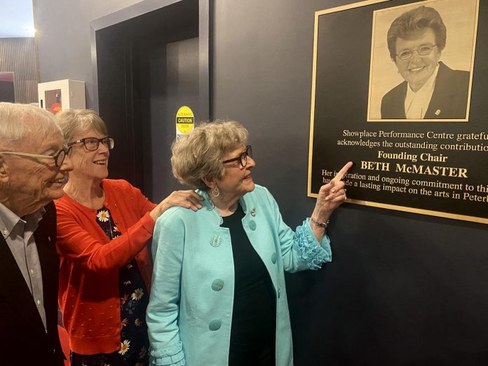 Beth McMaster, who was instrumental in the founding of Showplace Performance Centre in downtown Peterborough in the early 1990s and served as the inaugural chair of the non-profit organization's board of directors, points to the plaque honouring her contribution that was unveiled in the lobby of the performing arts venue on June 11, 2024. (Photo: Paul Rellinger / kawarthaNOW)