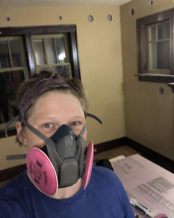 Peterborough homeowner Madeleine Endicott dons a mask to tackle the dusty job of patching up the drilled walls. After Hastings-based company New Energy Consulting Canada blew cellulose insulation innto the walls, the couple did all patchwork, sanding, and painting themselves. (Photo: Madeleine Endicott)