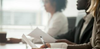 Three diverse people sitting at a boardroom table. (Stock photo)