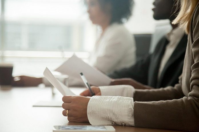 Three diverse people sitting at a boardroom table. (Stock photo)