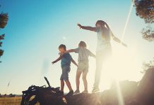 Three children outside in the warm weather balancing on a fallen tree near a field. (Stock photo)