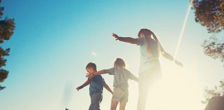 Three children outside in the warm weather balancing on a fallen tree near a field. (Stock photo)