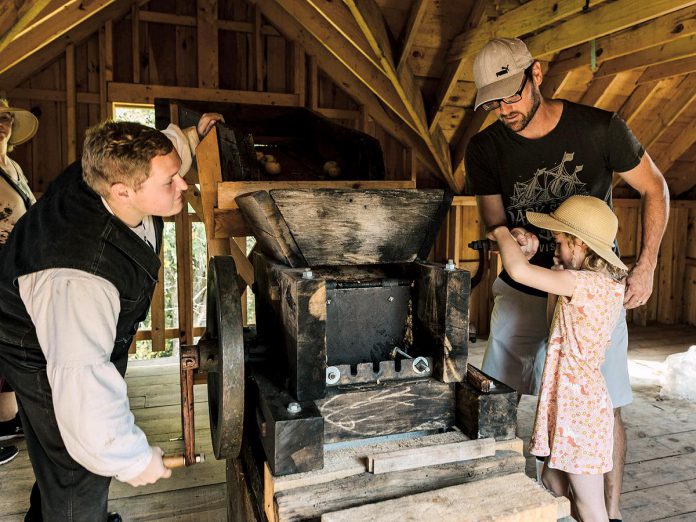 A young girl gets some help pressing apples for cider 19th-century style at the 2023 Applefest at Lang Pioneer Village Museum in Keene. The popular annual family event returns for 2024 on Sunday, October 7. (Photo: Heather Doughty Photography)