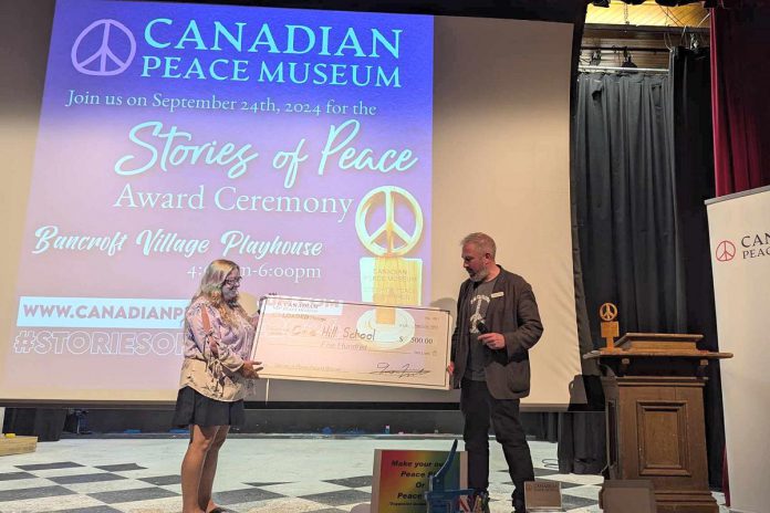 Angela Reid, office administrator of Coe Hill School, accepts a cheque for $500 from Chris Houston, founder of the Canadian Peace Museum, during the Stories of Peace Award ceremony on September 24, 2024 at Bancroft Village Playhouse. The school, which won the second annual ward for its video submission, also received a trophy and congratulatory scrolls from the federal and provincial governments. (Photo: Dave Raymond)