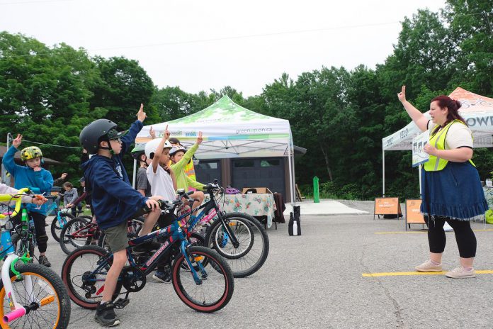 GreenUP active transportation program coordinator Ashley Burnie teaches students the 2-V-1 rule of fitting bike helmets during a Let's Bike event at Buckhorn Public School in June 2023. GreenUP has a long history of providing environmental stewardship programming for children, including promoting the health and environmental benefits of cycling. While 386 children took part in GreenUP's cycling education events in 2024, programming is now at risk. (Photo: Lili Paradi)