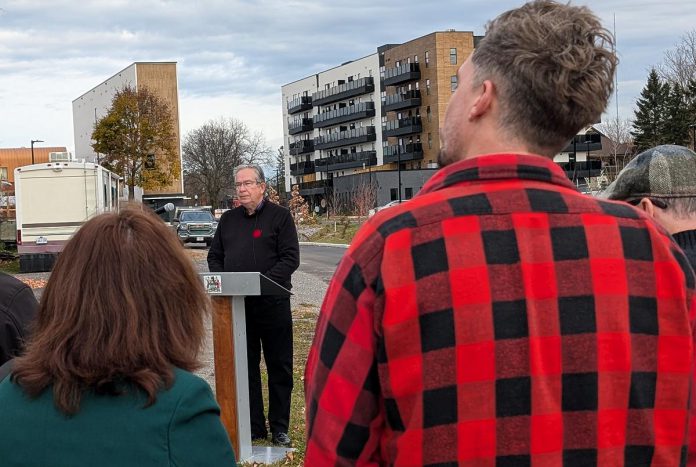 Peterborough city councillors Lesley Parnell and Alex Bierk listen as Peterborough Mayor Jeff Leal is asked a question during at a media event on November 5, 2024 in front of of Ashburnham Realty's six-storey building currently under construction along the Rotary Greenway Trail just north of Robinson Street in Peterborough's East City. Pictured in the background are two of the completed buildings in Ashburnham Realty's three-building residential-commercial development. (Photo: Bruce Head / kawarthaNOW)