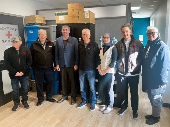 Dr. John Beamish and Dr. Yosra AlMakadma (fourth and fifth from left) are two of the physicians involved in Peterborough Street Medicine, which will receive over $1 million per year over three years to provide primary health care and mental health services to people in Peterborough who are homeless or underhoused through an alternate funding plan agreement. Also pictured from left to right are Peterborough city councillor Keith Riel, mayor Jeff Leal, Peterborough-Kawartha MPP Dave Smith, and city councillors Alex Bierk and Joy Lachica. (kawarthaNOW composite photo via Alex Bierk / Office of Dave Smith)