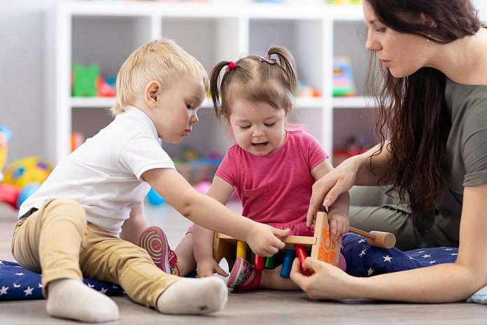 Two young children and an early childhood educator. (Stock photo)