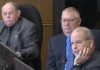 At Peterborough city council's general committee meeting on January 6, 2025, councillor Kevin Duguay (right) asks a question of city staff while councillors Keith Riel and Gary Baldwin look on during a discussion of a staff report recommending the city expand the modular bridge housing community at Wolfe Street by up to 16 cabins, if the city is successful in its application for $1.3 million in funding from two new provincial programs. The councillors were three of the six who voted in favour of the staff report, with five voting against. (kawarthaNOW screenshot of City of Peterborough video)