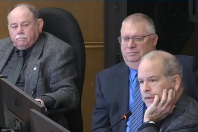 At Peterborough city council's general committee meeting on January 6, 2025, councillor Kevin Duguay (right) asks a question of city staff while councillors Keith Riel and Gary Baldwin look on during a discussion of a staff report recommending the city expand the modular bridge housing community at Wolfe Street by up to 16 cabins, if the city is successful in its application for $1.3 million in funding from two new provincial programs. The councillors were three of the six who voted in favour of the staff report, with five voting against. (kawarthaNOW screenshot of City of Peterborough video)