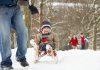 A winter scene showing a man pulling a young boy on a sled with a young girl and boy walking in the background. (Stock photo)