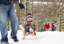 A winter scene showing a man pulling a young boy on a sled with a young girl and boy walking in the background. (Stock photo)