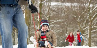 A winter scene showing a man pulling a young boy on a sled with a young girl and boy walking in the background. (Stock photo)