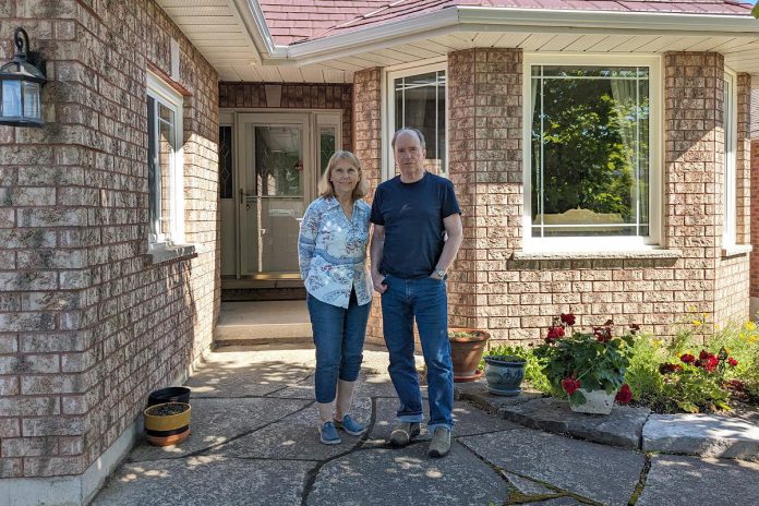 Michael and Norma Doran stand in front of their fully electrified Peterborough home, which includes an air source heat pump and a heat pump water heater. (Photo: Clara Blakelock / GreenUP)