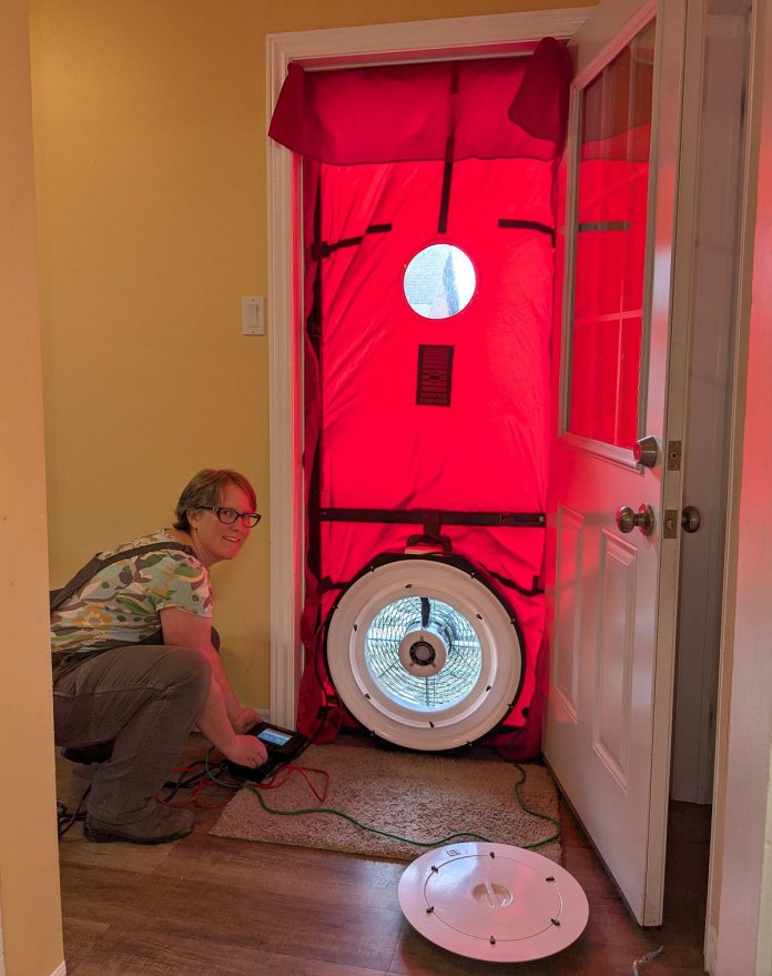 Clara Blakelock, the article's author and GreenUP registered energy advisor, sets up a blower door as part of an EnerGuide home energy assessment. GreenUP's Heat Pump Advisory Service starts with an EnerGuide evaluation, which gives the homeowner a clear picture of how their home uses energy, and where upgrades can be beneficial. (Photo: Clara Blakelock / GreenUP)