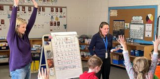 Five Counties clinicians Katy Morton (left) and Emily Vann get first and second graders at St. Joseph's Catholic Elementary School in Douro to stretch and show how "tallies" (letters like t, f, and b) differ from others in the alphabet. The exercise aims to reinforce proper printing techniques for the students. (Photo courtesy of Five Counties)