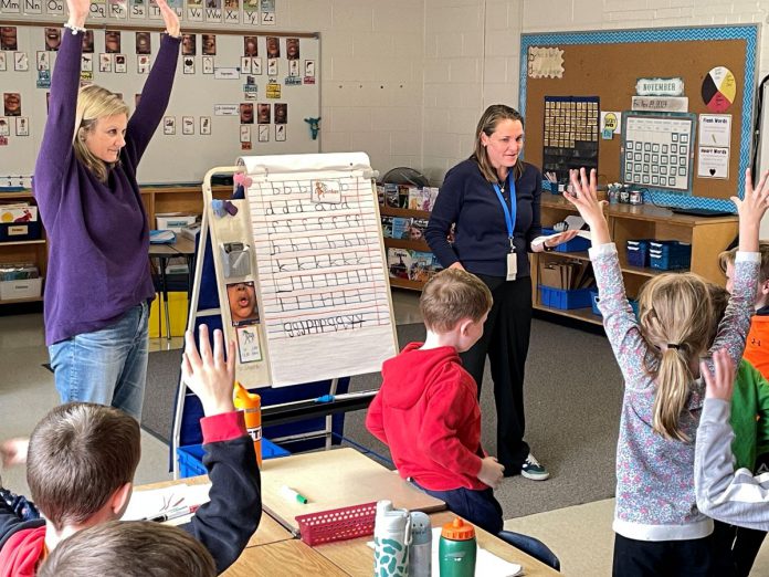 Five Counties clinicians Katy Morton (left) and Emily Vann get first and second graders at St. Joseph's Catholic Elementary School in Douro to stretch and show how "tallies" (letters like t, f, and b) differ from others in the alphabet. The exercise aims to reinforce proper printing techniques for the students. (Photo courtesy of Five Counties)