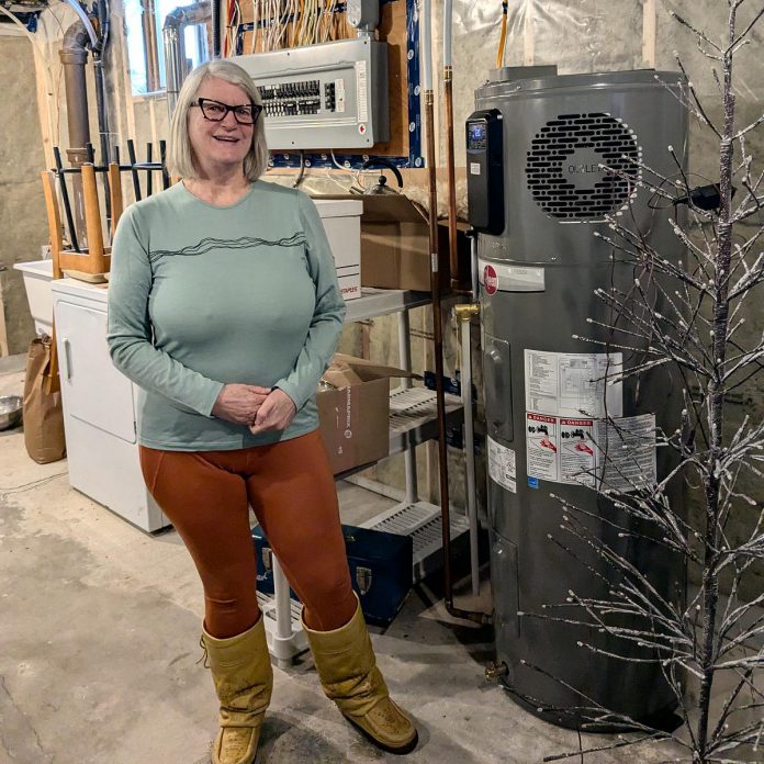 In place of a gas furnace, Madeleine Pengelley and David Pritchard's home in Peterborough's East City is heated by a heat pump connected to a central air handler located in the basement. Pengelley stands in their newly insulated basement next to their heat pump hot water heater, which uses heat pump technology to extract heat from the indoor air to very efficiently heat the water. (Photo: Clara Blakelock / GreenUP)