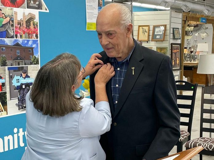 Susan Zambonin, CEO of Habitat for Humanity Peterborough & Kawartha Region (Habitat PKR), pins the King Charles III's Coronation Medal on the jacket of Harry Pearson, who received the award along with Cindy Windover in recognition for their volunteer work with the organization during a celebration at the Lakefield ReStore on March 6, 2025. (Photo: Habitat PKR)