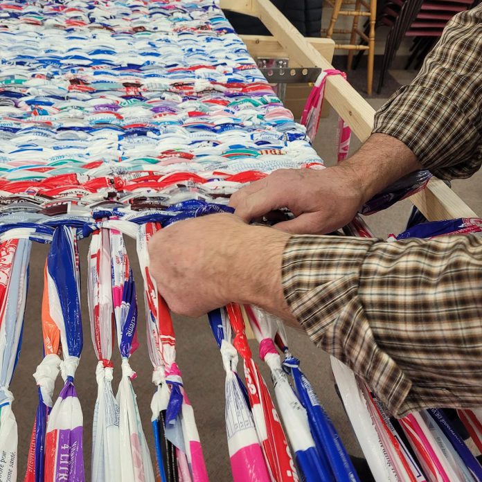 To transform plastic milk bags into sleeping mats, the volunteers link seven milk bags together, held taught by nails on either side of the loom, and then cross weave rows of bags over two links at a time. The two looms were built by church group organizer Tim Young, who learned how to turn milk bags into sleeping mats on mission trips to Haiti. (Photo: Street Level Advocacy / Facebook)