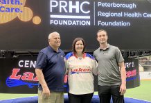 Flanked by Peterborough Century 21 Lakers board member Len Powers (left) and player Dylan Hutchison (right), Peterborough Regional Health Centre (PRHC) Foundation president and CEO Lesley Heighway dons a Peterborough Century 21 Lakers jersey at the Peterborough Memorial Centre on May 12, 2025 for an announcement of a partnership between the Lakers and the PRHC Foundation to support the $60 million Campaign for PRHC. (Photo courtesy of Peterborough Century 21 Lakers)