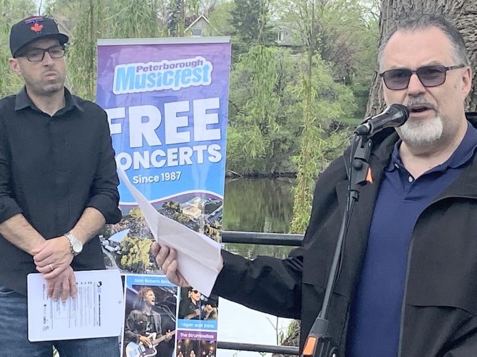 Peterborough Musicfest board chair Brian Ellis (right) speaks during the 38th season lineup reveal at The Silver Bean Café in Millennium Park on May 15, 2025 as emcee Vince Bierworth looks on. (Photo: Paul Rellnger / kawarthaNOW)