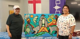 Former Nogojiwanong Friendship Centre board vice-president and president David Newhouse and Georgie Horton-Baptiste pictured in July 2024 with artwork by Indigenous artist Jared Tait. The non-profit organization in Peterborough is inviting community members to a gathering on June 20, 2025 to commemorate National Indigenous Peoples Day the following day. (Photo: Nogojiwanong Friendship Centre / Facebook)