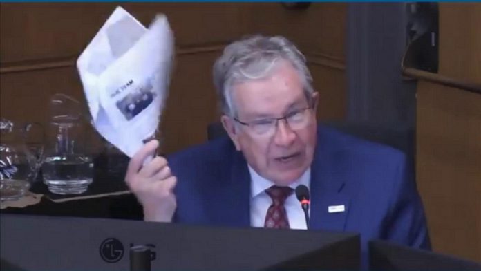 Peterborough mayor Jeff Leal gestures with the 2024-25 annual report of One City Peterborough during a general committee meeting on June 23, 2025, indicating he didn't support providing additional funding to the non-profit organization that operates services for homeless people at Trinity Centre. (kawarthaNOW screenshot of City of Peterborough video)