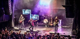 Retro rock tribute band Neon Nostalgic (Shawn Brady, Kevin Strom, Grant Strom, and John Johnstone) performs a free-admission concert in Del Crary Park on July 1, 2025 for the Canada Day edition of Peterborough Musicfest. The band performs hits from the 1980s and 1990s in synch with the artists' original music videos for the songs they perform. (Photo: Serrano Photography Studios)