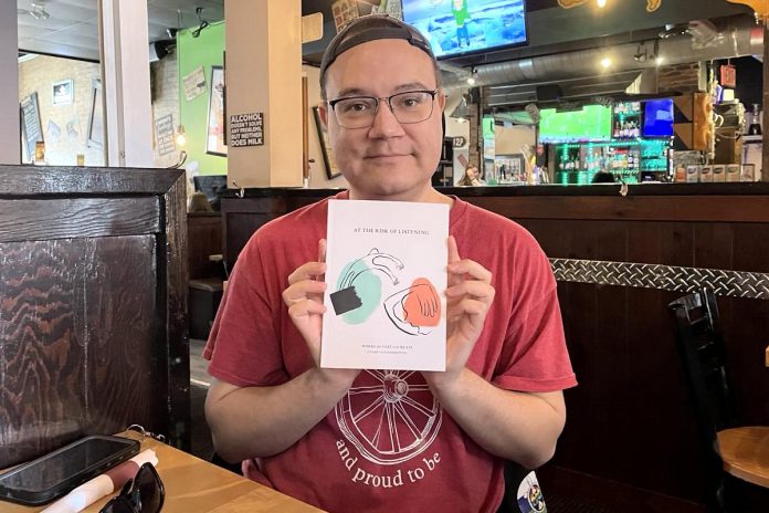 A friend of poet Ziysah von Bieberstein, Bren Aisaican Henderson holds a copy of Ziysah's "At the Risk of Listening," a 65-page, three-section collection of poetry, speeches, addresses, and other work written and presented by Ziysah during their time as the City of Peterborough's second poet laureate. The book will be launched on June 13 and 14, 2025 at Peterborough's Take Cover Books. (Photo: Ziysah von Bieberstein)